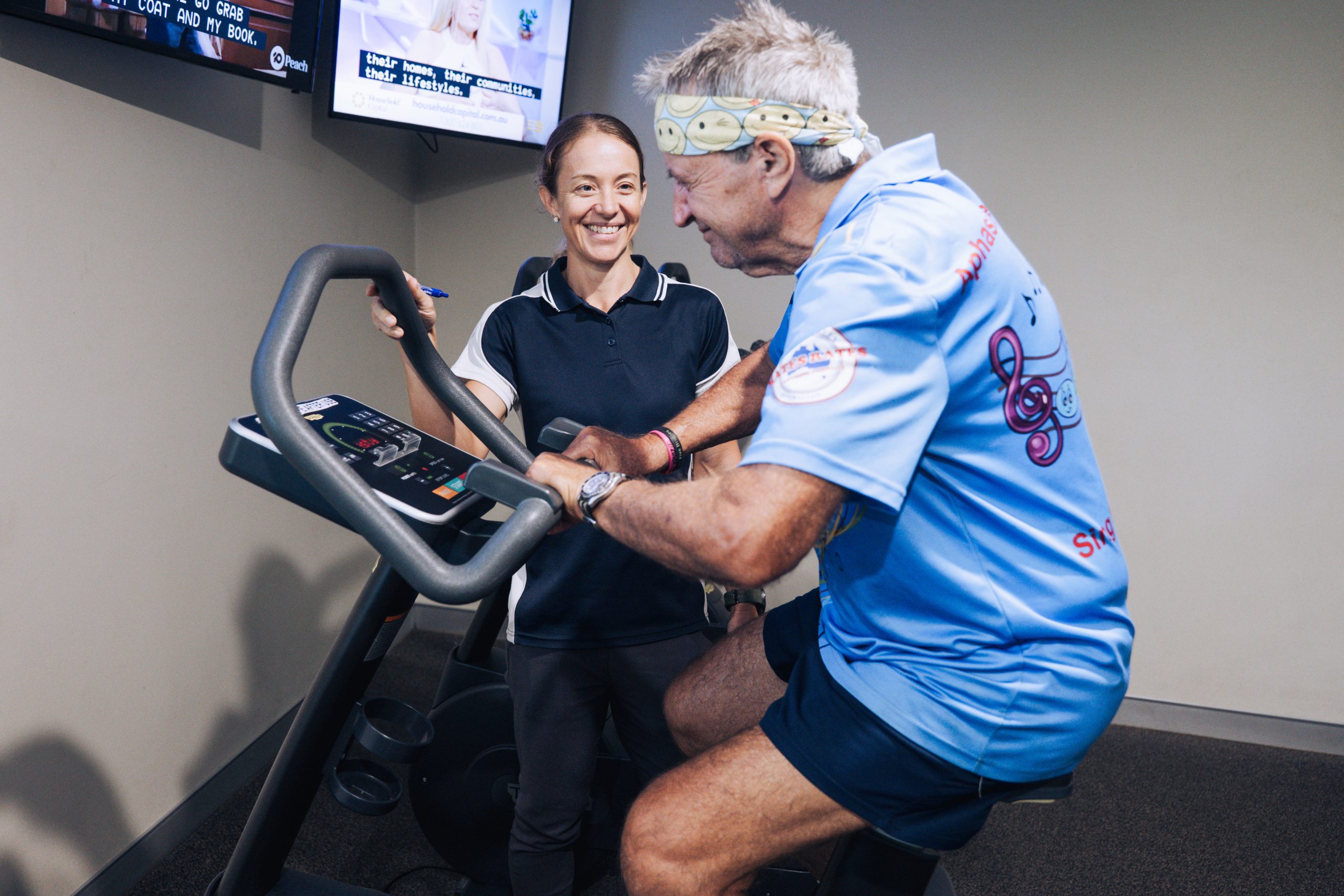 Exercise Physiologist smiles while supporting her patient on gym equipment