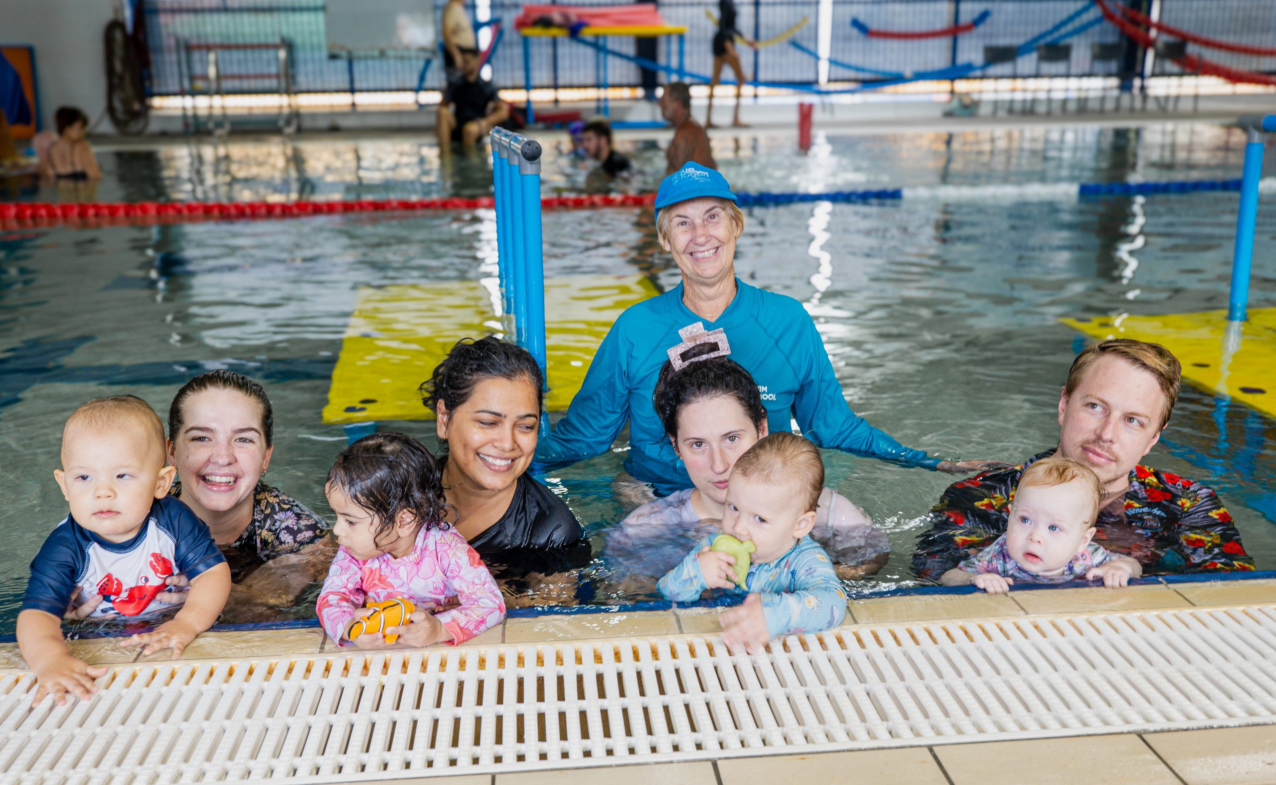 Logan Swim School tutor standing behind four parents holding babies in the water.